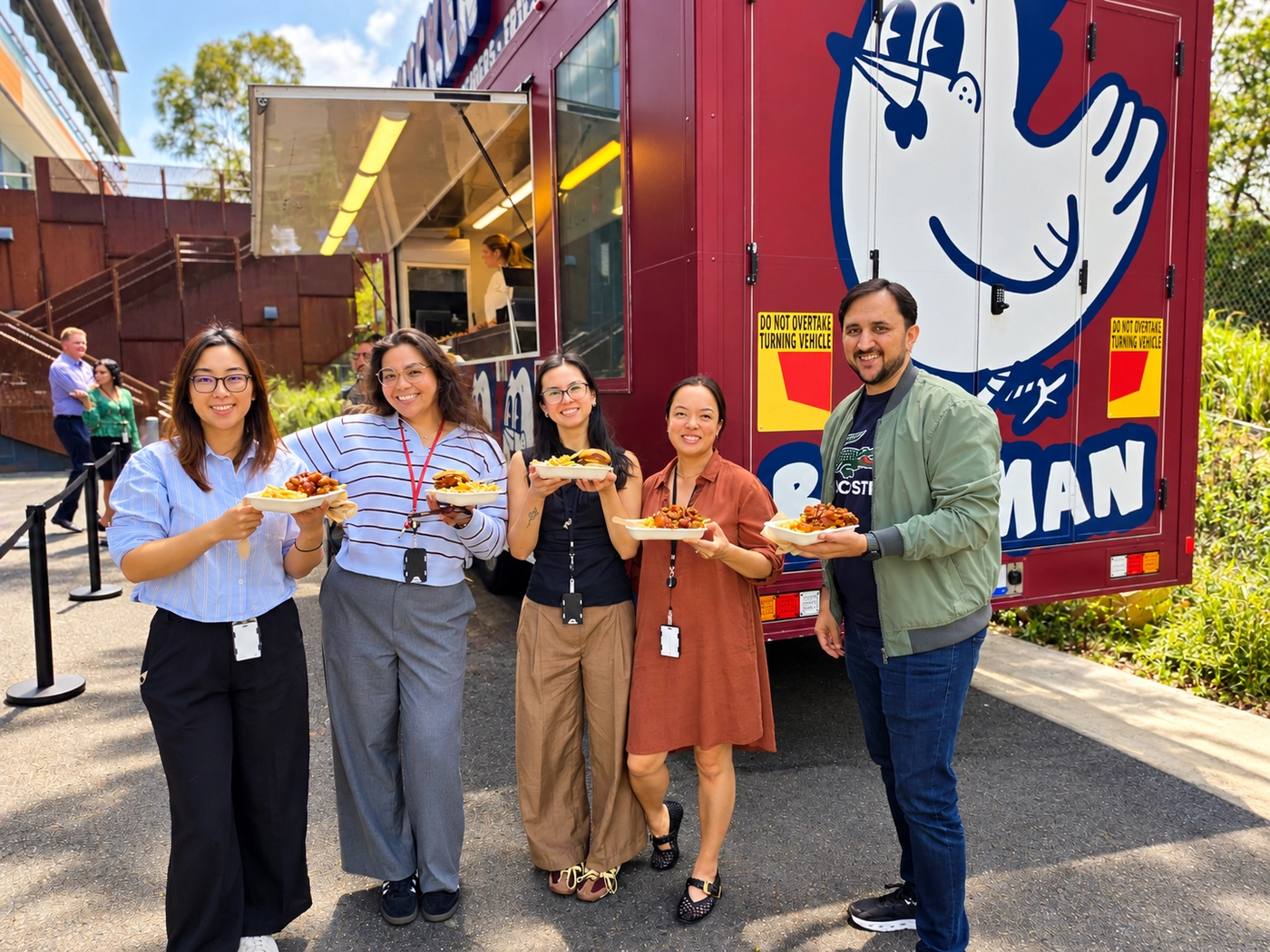 Five office workers holding boxes of Korean fried chicken, burgers and fries in front of the Birdman food truck at a corporate event in Sydney