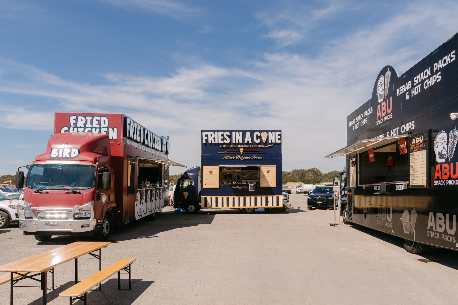 Three Food Hub food trucks, Birdman fried chicken, Nillas Belgian fries and Abu Snack Packs, set up side by side with bench seating on a site in Sydney