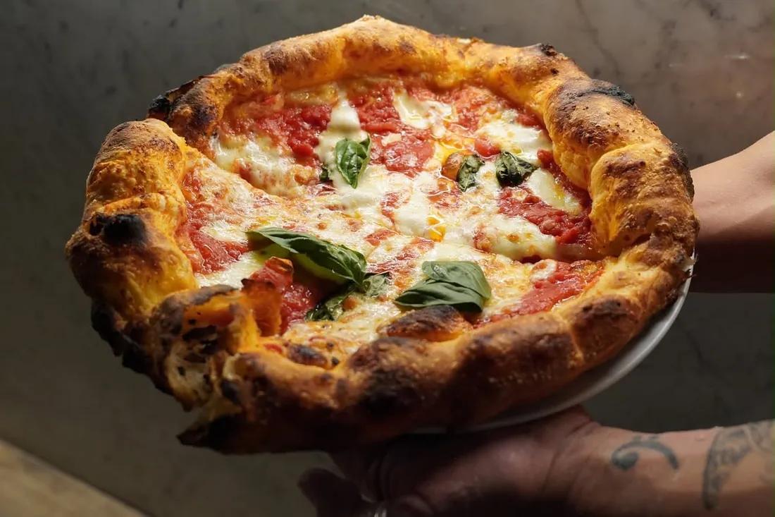 Margherita pizza with a puffy blistered crust, mozzarella and fresh basil, held up straight from the oven