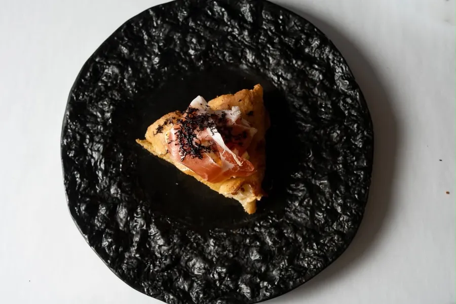 Slice of prosciutto and shaved truffle pizza on a black plate