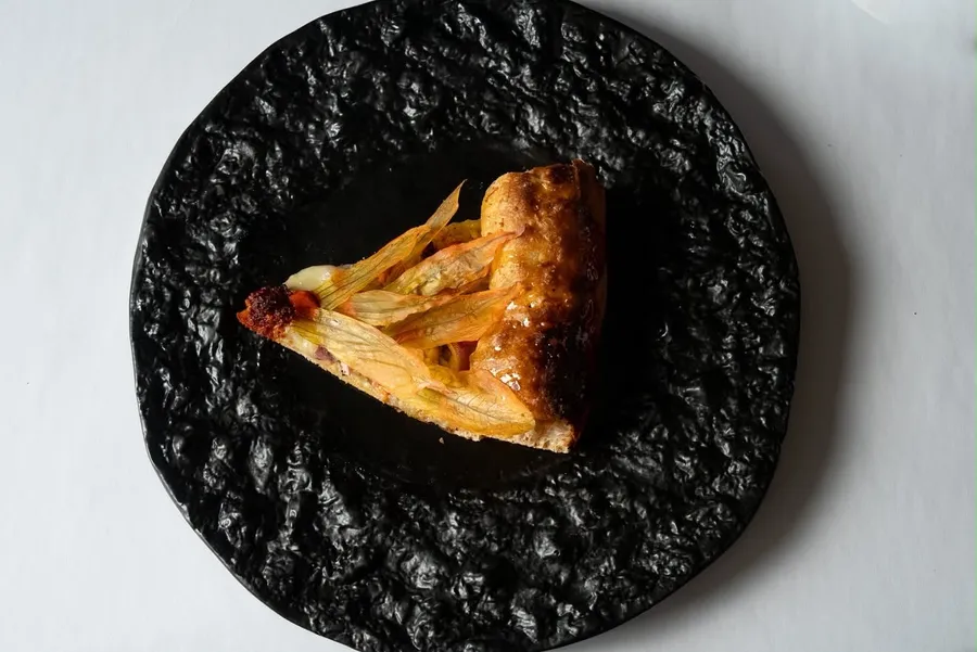Slice of zucchini flower pizza on a black plate