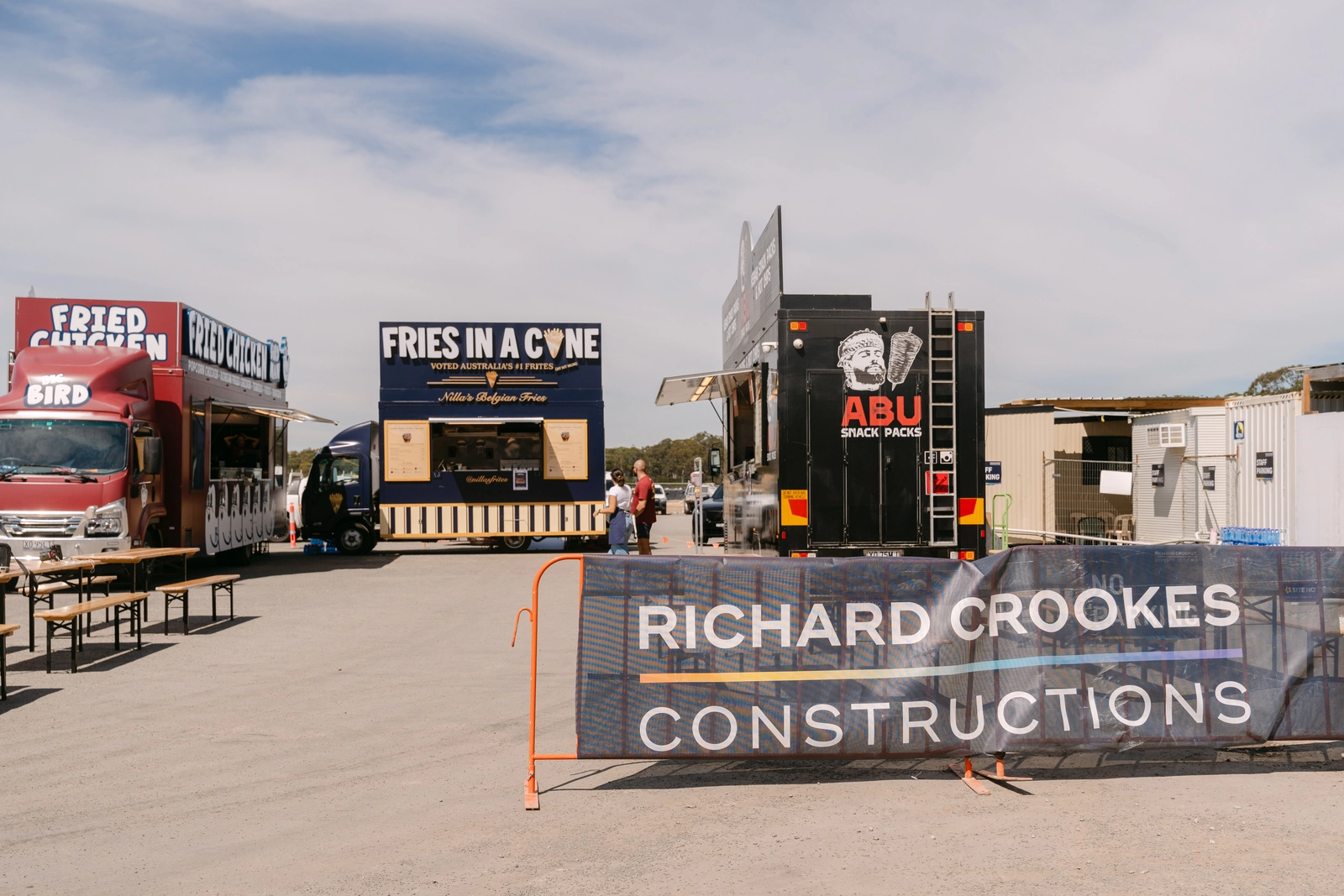 Three Food Hub trucks parked inside a Richard Crookes Constructions site compound in Moorebank before service, with the builder's banner on the fence